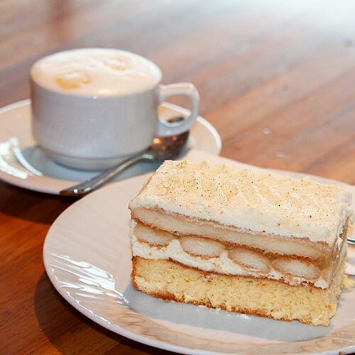 Ein Stück ApfelTiramisuschnitte mit einer Tasse Melange im Hintergrund