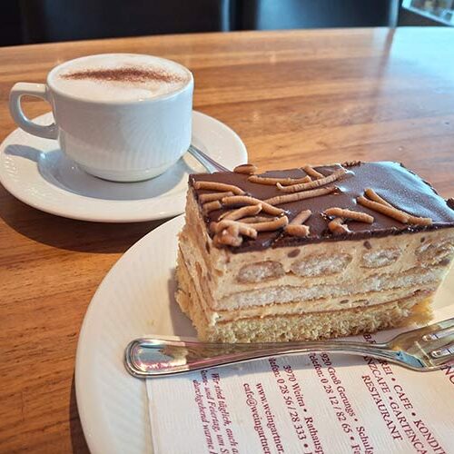 Eine Maroni-Tiramisu-Schnitte vor einer Tasse Melange.