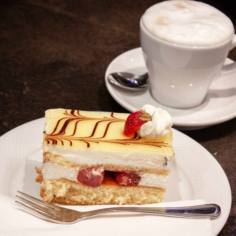 eine Tasse Melangekaffee und ein Teller mit einer Erdbeer Zitronen Schnitte