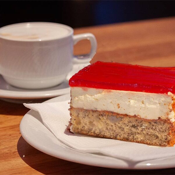 Ein Teller mit einem Stück Topfen-Mohn-Schnitte vor einer Tasse Kaffee