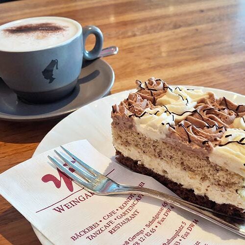 Ein Stück Haselnuss-Schoko Schnitte mit einer Tasse Kaffee.